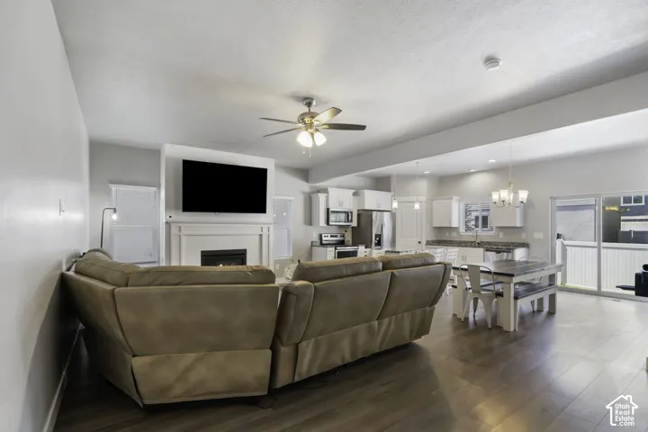 Open-concept living space featuring wood-finish flooring, a ceiling fan with integrated lighting, and a fireplace with a mantel