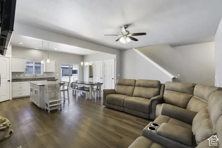 Open-concept living area featuring wood-finish flooring, a contemporary ceiling fan, and a light-filled kitchen with white cabinetry and granite countertops