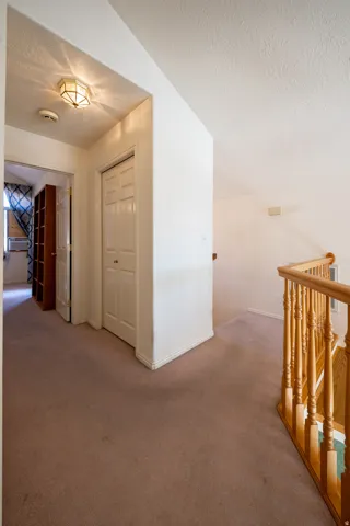 Carpeted hallway with a wood spindle railing and recessed lighting