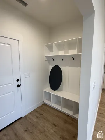 Built-in white storage cabinetry featuring upper cubbies, lower shelving units, and matte black wall hooks, complemented by wood-finish flooring