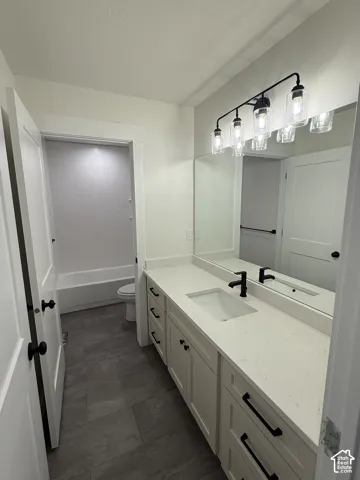 Bathroom featuring a vanity with a quartz countertop, an integrated rectangular sink, matte black hardware, and an industrial-style light fixture
