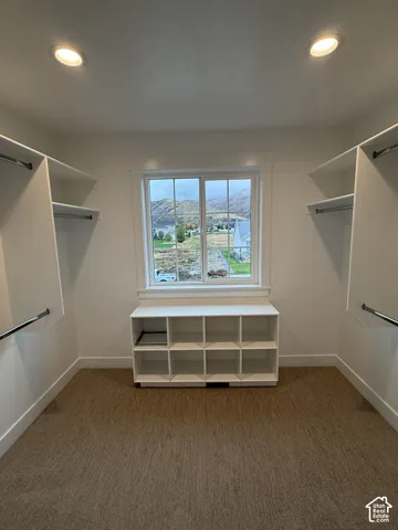 Custom walk-in closet featuring white built-in shelving, hanging rods, recessed lighting, and a window with mountain scenery