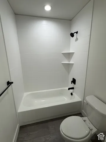 Full-height tub and shower surround with white rectangular tile, matte black fixtures, integrated corner shelving, and large-format tile flooring