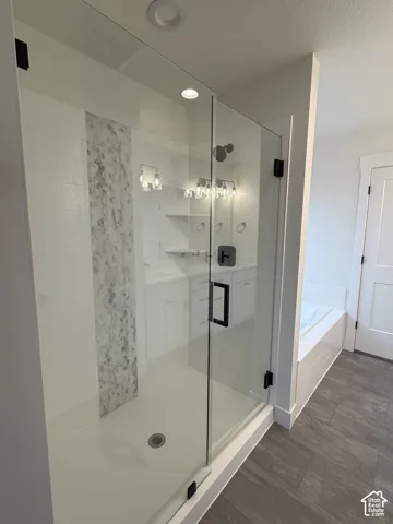 Walk-in shower featuring a frameless glass door, matte black hardware, and vertical decorative tile inlay, accompanied by a soaking tub and wood-finish tile flooring