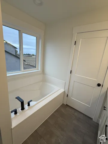 Built-in soaking tub with matte black fixtures, wood-finish tile flooring, and a two-panel interior door