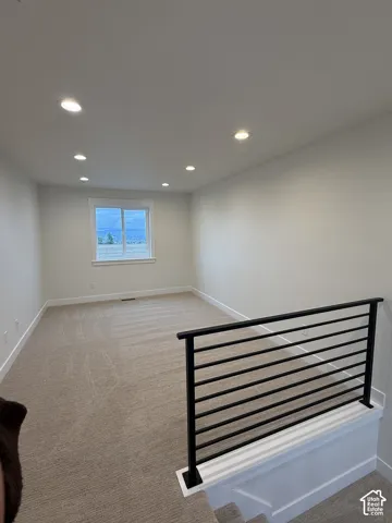 Neutral-toned carpeting, recessed ceiling lighting, and a modern black metal horizontal railing