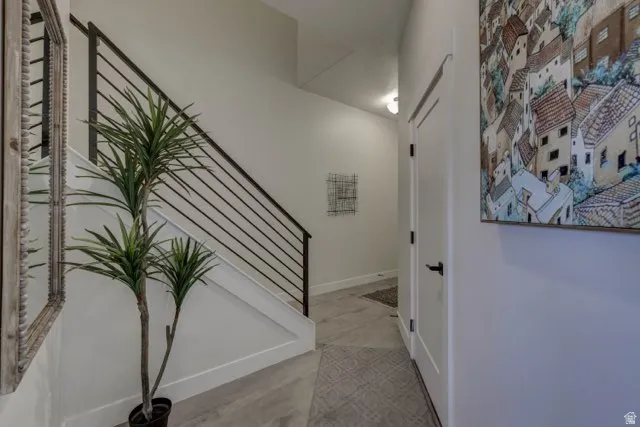 Modern hallway featuring a floating staircase with horizontal metal railings, light wood-finish flooring, and clean white walls