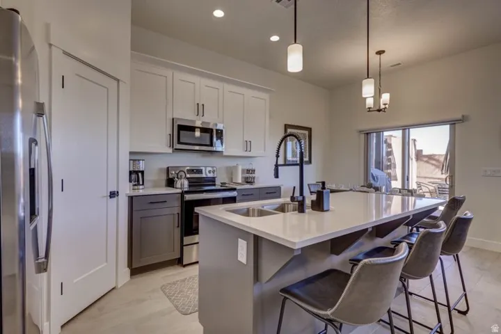 Modern kitchen featuring stainless steel appliances, a large island with sink, pendant lighting, two-tone cabinetry, and wood-finish flooring