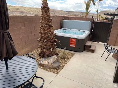 Patio featuring a built-in hot tub with cover, concrete paving, and a decorative rock garden with a mature palm