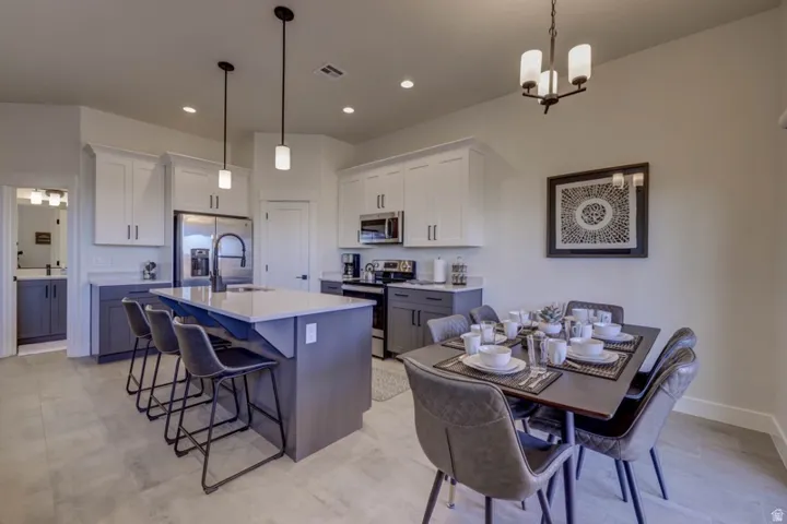 Open-concept kitchen and dining area featuring a kitchen island with seating, stainless steel appliances, white upper cabinetry, and gray lower cabinetry