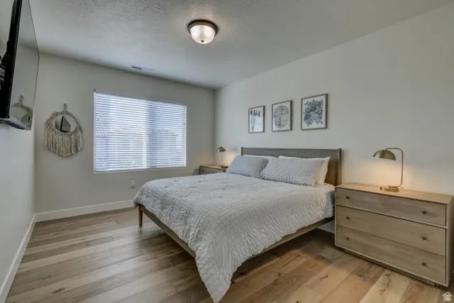 Bedroom featuring wood-finish flooring, a contemporary ceiling light fixture, and a large window with blinds