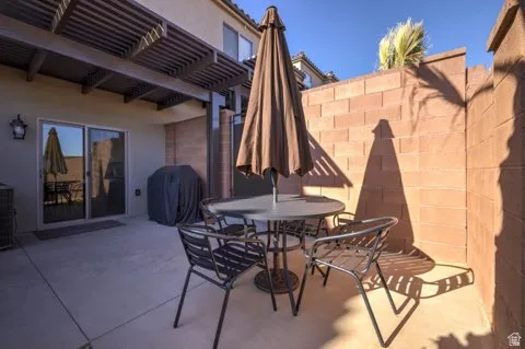 Private concrete patio featuring a slatted pergola overhead