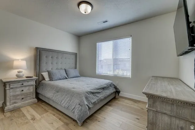 Bedroom featuring light wood-finish flooring, white walls, and a single window with blinds