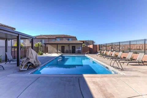 Community swimming pool featuring a concrete deck, metal perimeter fencing, and a covered lounge area