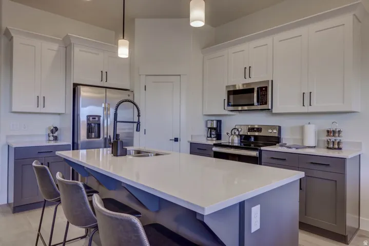 Modern kitchen featuring a central island with integrated sink, two-tone cabinetry, stainless steel appliances, and pendant lighting