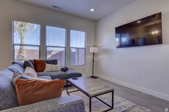 Living area featuring three large windows with blinds, recessed lighting, and wood-finish flooring