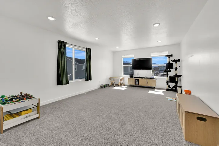 Spacious loft room featuring light gray carpeting and white walls, lots of natural light