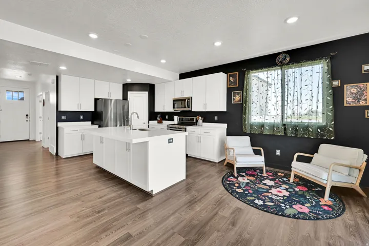 Open-concept kitchen and living area featuring LVP flooring, white cabinetry, a kitchen island with seating, stainless steel appliances, and recessed lighting