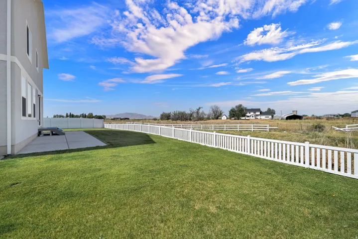 Expansive backyard featuring a manicured lawn, white picket fencing, and a concrete patio