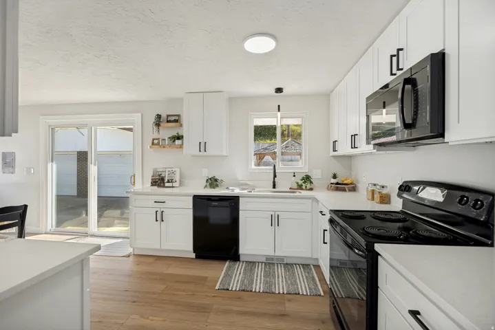 Modern kitchen featuring white cabinetry, black hardware, solid surface countertops, and wood-finish flooring