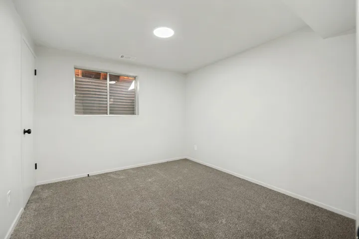 Carpeted room featuring white walls, a recessed ceiling light, and a single window with a corrugated metal window well