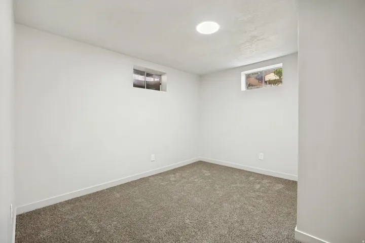 Carpeted interior space featuring light gray walls, two high-set windows, and a circular ceiling light fixture