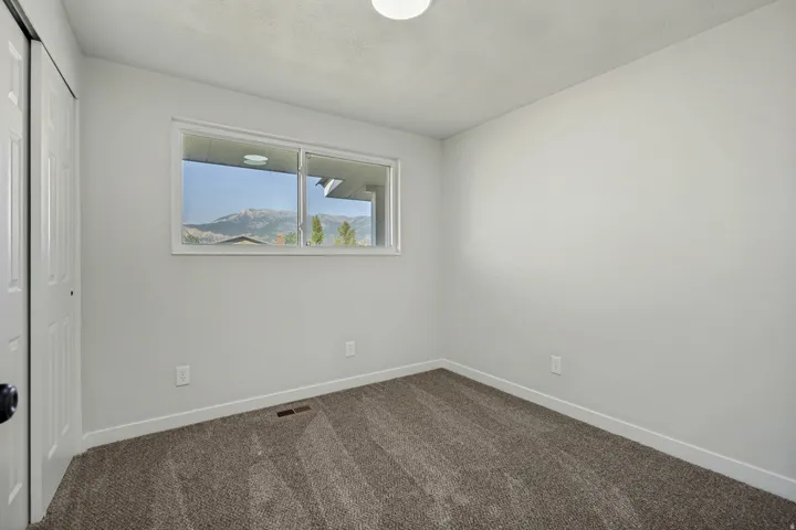 Room featuring a window with mountain scenery, neutral-toned walls, gray carpet flooring, white baseboards, and a bi-fold closet door