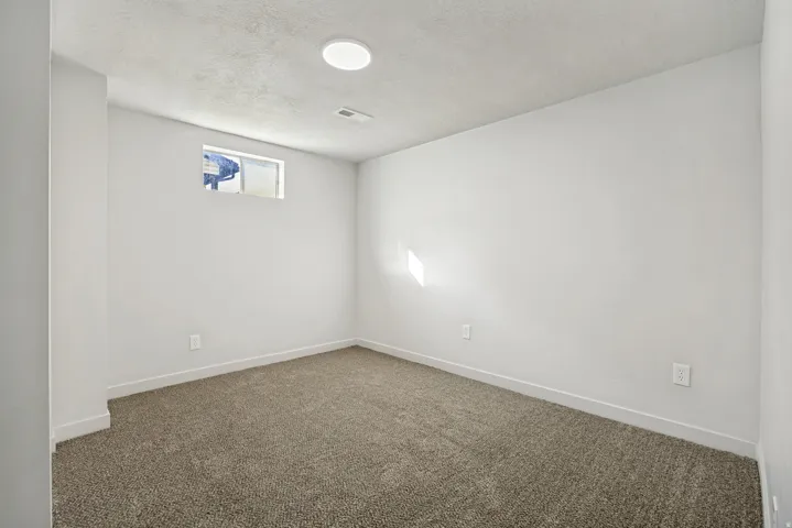 Neutral-toned carpeting featuring white baseboards, a single light fixture, and a high-set window