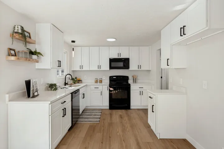 U-shaped kitchen featuring white cabinetry, black hardware, wood-finish flooring, a black appliance suite, and light-toned countertops