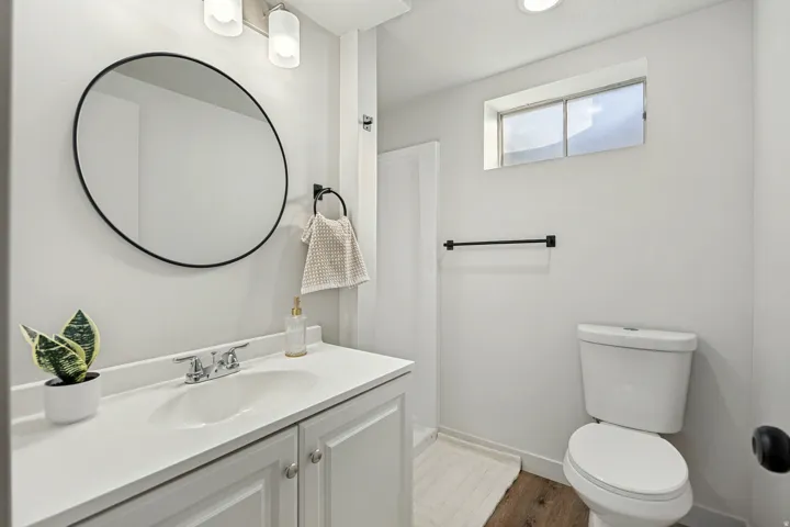 Bathroom featuring a white vanity with an integrated sink, polished chrome faucet, and a round black-framed mirror