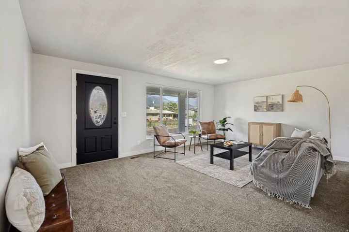 Spacious living area featuring neutral carpeting, white walls, large windows, and a black front entry door with an oval glass insert