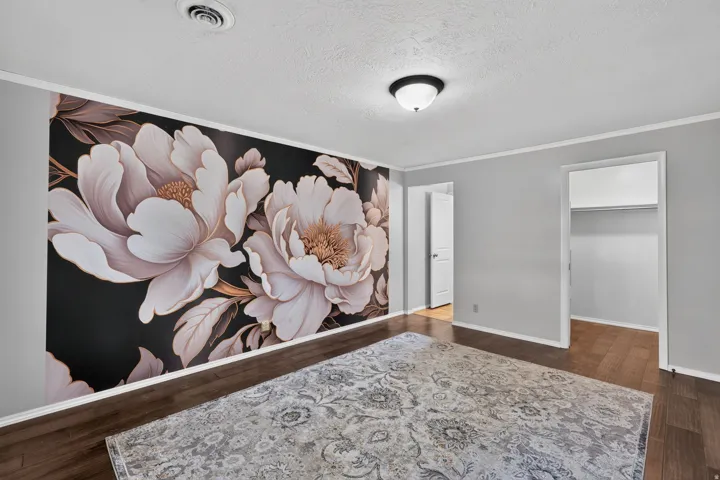 Spacious room featuring a floral accent wall, wood-finish flooring, and light gray painted walls