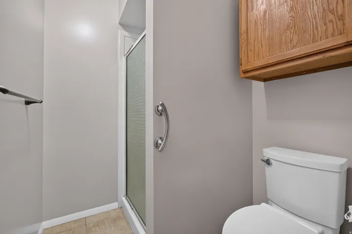 Full bathroom featuring a white toilet, enclosed shower with a frosted glass door, and tile flooring