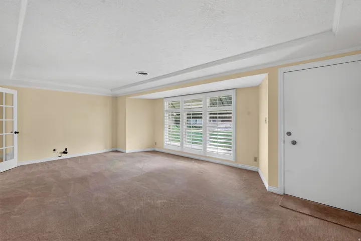 Recessed ceiling with layered trim, bay window with plantation shutters, French doors, and neutral carpeting
