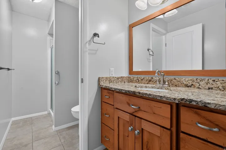 Bathroom vanity featuring a wood-finish cabinet with chrome hardware, a granite countertop, and an undermount sink with a chrome faucet