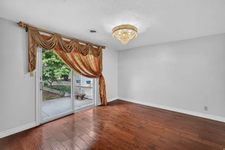 Sliding glass door opening to a concrete patio, complemented by rich wood-finish flooring and a decorative ceiling light fixture