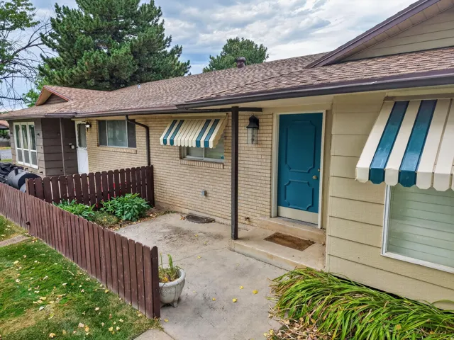 Exterior featuring a teal entry door, light brick facade, and striped awnings over windows