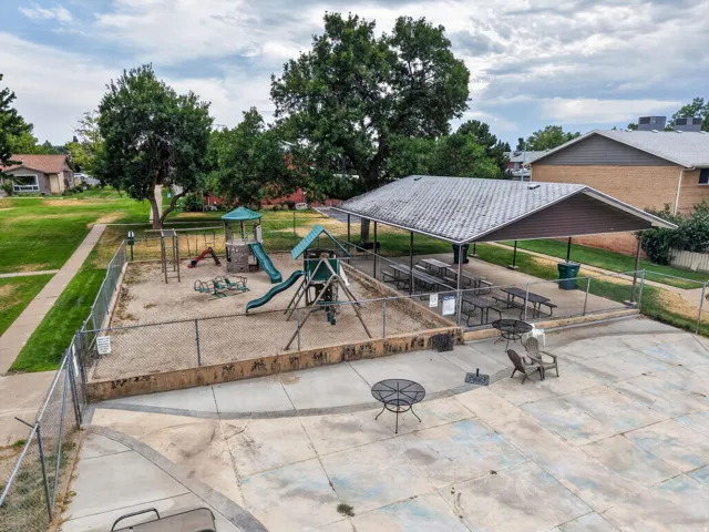 Community recreation area featuring a fenced sandbox play structure, covered picnic tables, and an expansive concrete patio