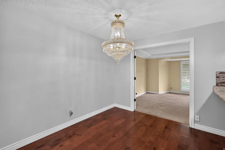 Elegant crystal chandelier illuminating a room with wood-finish flooring, light gray walls, and white baseboards