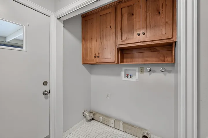 Laundry area featuring wood cabinetry with storage, white tiled flooring, and an exterior door with frosted glass