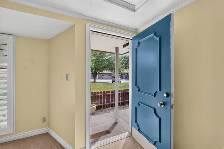 Entryway featuring a decorative blue door with chrome hardware, neutral-toned walls, white crown molding, and plantation shutters