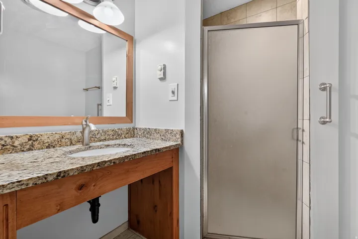 Bathroom featuring a wood vanity with a granite-style countertop and integrated sink, a large framed mirror, and a frosted glass shower enclosure with a chrome grab bar