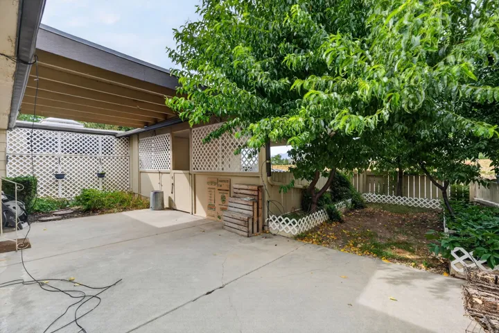 Covered patio area featuring a concrete slab, lattice privacy screens, and mature trees