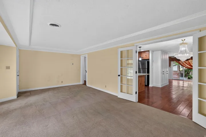 Carpeted living area with crown molding and direct access to a kitchen area featuring wood-finish flooring, a built-in breakfast bar, and white built-in storage cabinetry