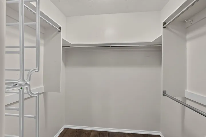 Spacious closet featuring wood-finish flooring, white baseboards, and multiple hanging rods for ample storage
