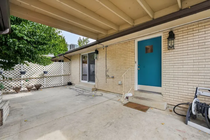 Covered concrete patio with a light brick exterior and an accent entry door