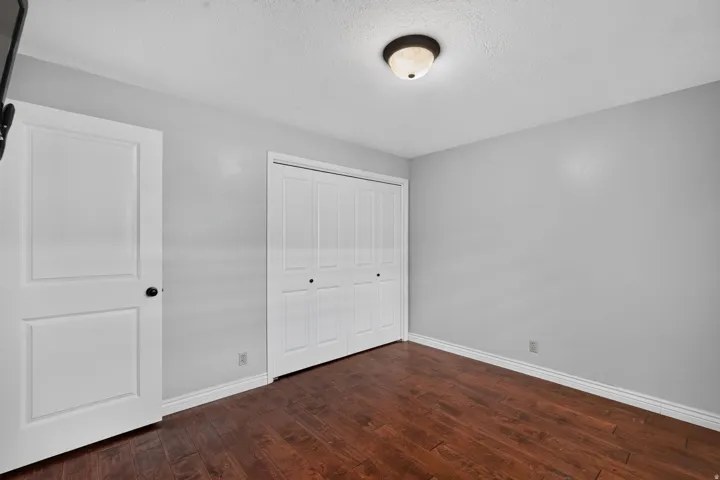 Room featuring wood-finish flooring, light gray walls, white baseboards, and a bi-fold closet