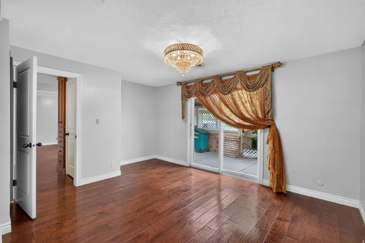 Spacious room featuring rich wood-finish flooring, a decorative chandelier, and light gray wall paint