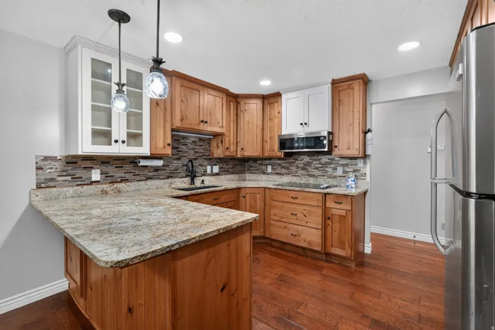 Kitchen featuring wood cabinetry, light-toned countertops, a mosaic tile backsplash, and stainless steel appliances