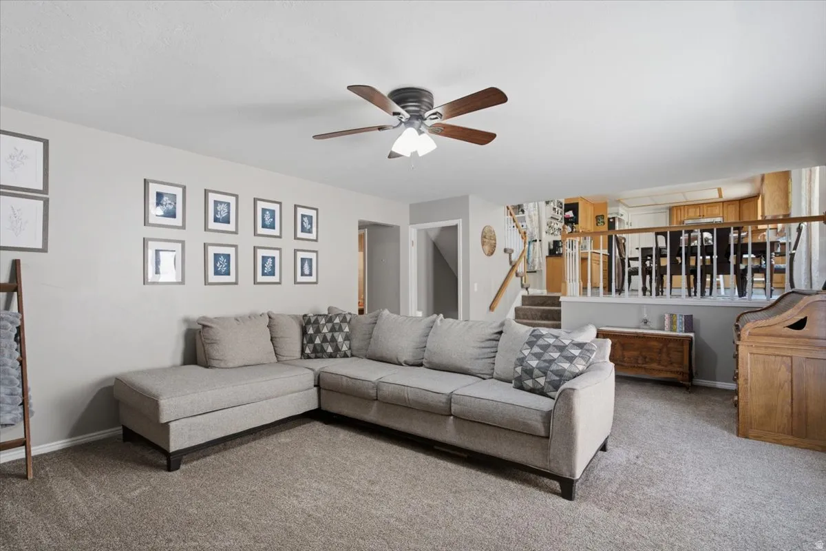 Spacious living area featuring neutral-toned carpet, a ceiling fan with integrated lighting, and light gray wall paint